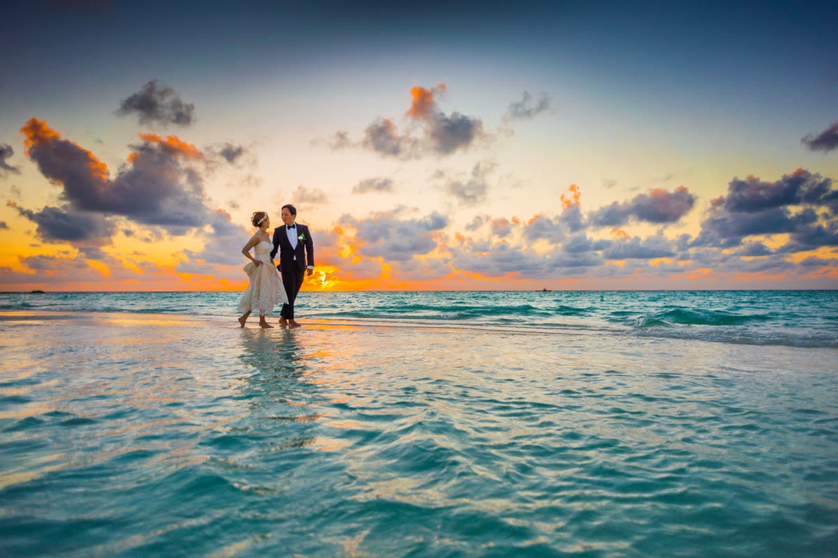 Newlywed couple walking on a tropical beach at sunset